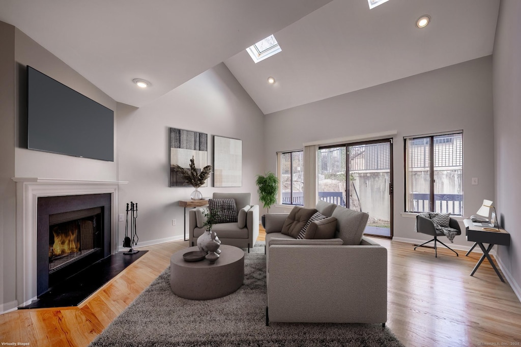 living room with light wood-type flooring, high vaulted ceiling, and a skylight