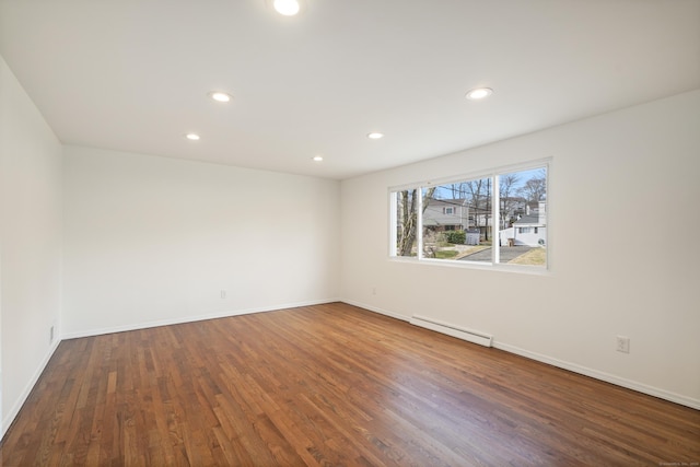 spare room featuring baseboard heating and dark wood-type flooring