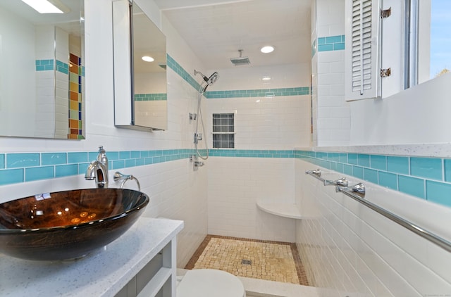 bathroom featuring toilet, a tile shower, tile walls, and vanity