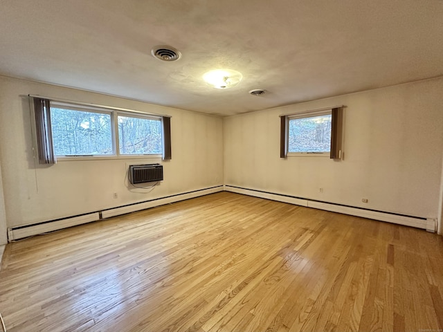 empty room with plenty of natural light, a wall mounted AC, and light hardwood / wood-style flooring