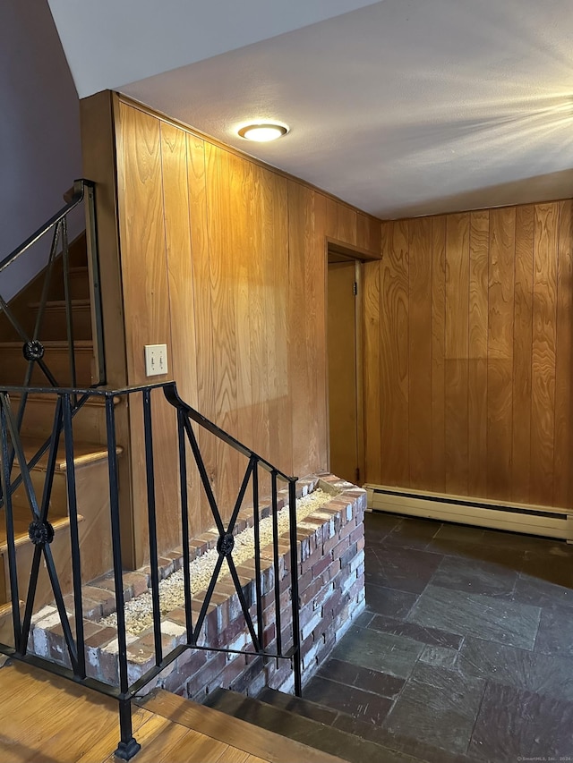 stairway with wood walls, wood-type flooring, and a baseboard radiator