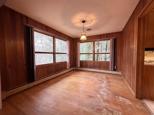 unfurnished dining area featuring wooden walls, light hardwood / wood-style floors, and a baseboard heating unit