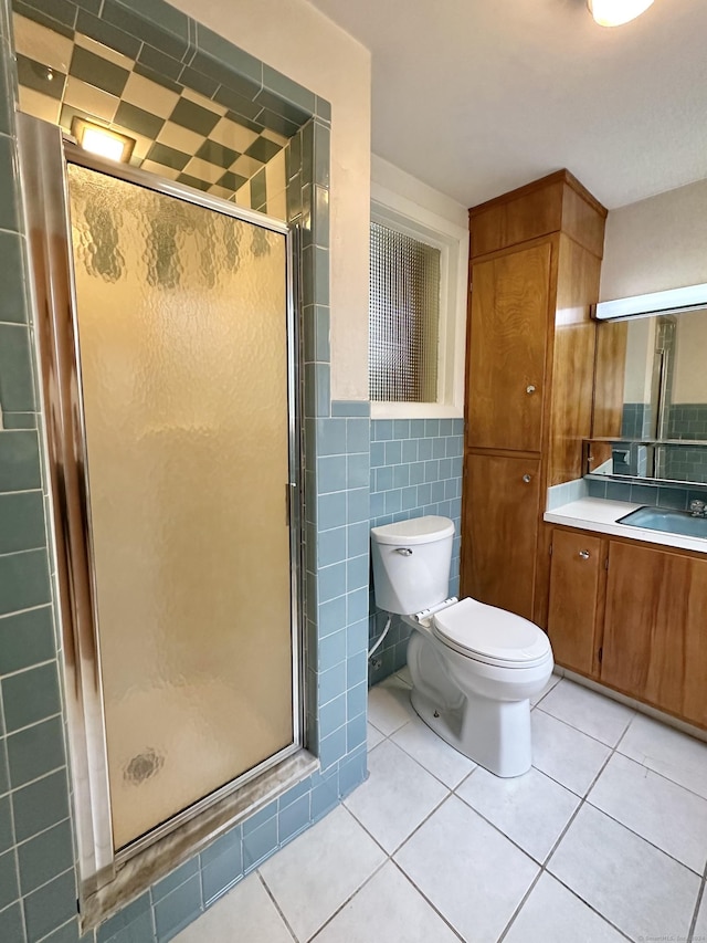 bathroom with vanity, a shower with door, tile patterned flooring, toilet, and tile walls