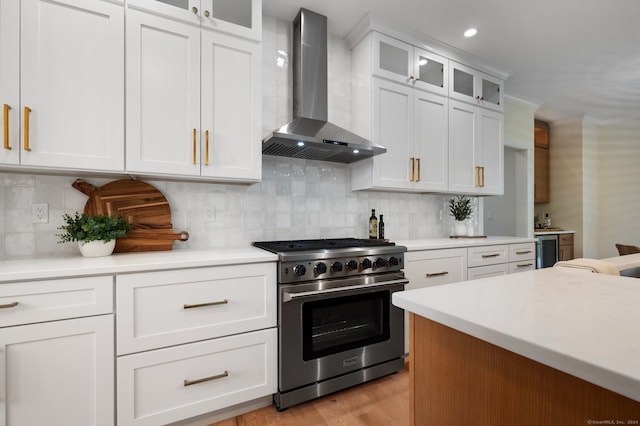 kitchen with light wood-type flooring, tasteful backsplash, wall chimney range hood, high end stainless steel range, and white cabinetry