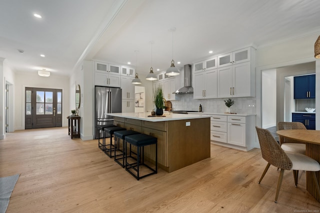 kitchen featuring a kitchen island, wall chimney range hood, pendant lighting, white cabinetry, and stainless steel refrigerator