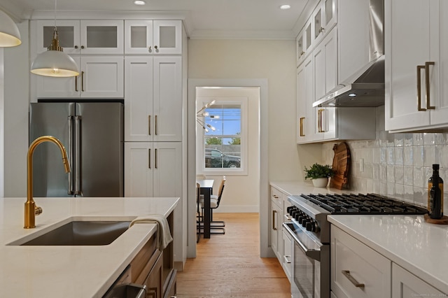 kitchen featuring sink, wall chimney exhaust hood, pendant lighting, high quality appliances, and white cabinets