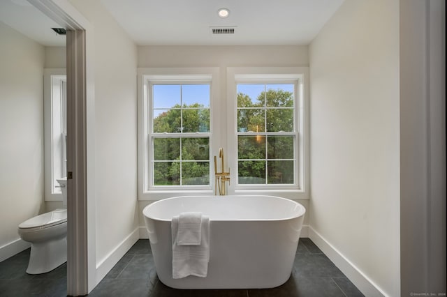 bathroom featuring a tub to relax in, tile patterned floors, and toilet