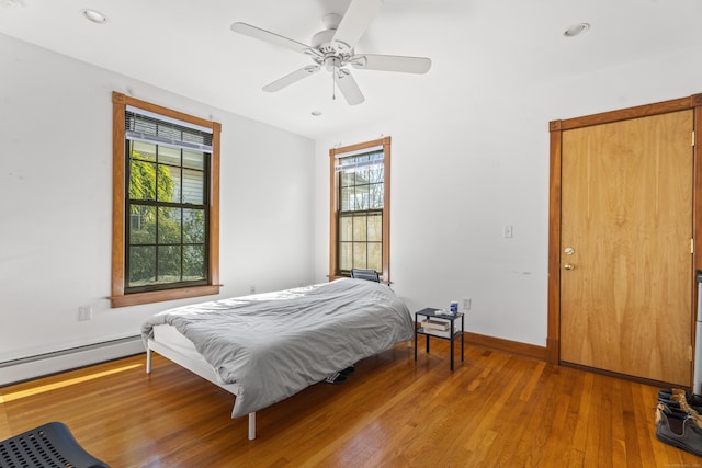 bedroom with ceiling fan, hardwood / wood-style floors, and a baseboard heating unit