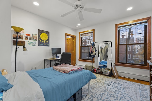 bedroom with ceiling fan, wood-type flooring, baseboard heating, and multiple windows