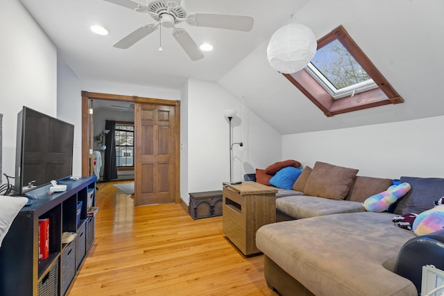 living room with light wood-type flooring, ceiling fan, and vaulted ceiling with skylight