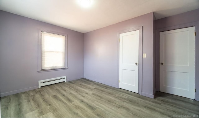 unfurnished bedroom featuring a closet, baseboard heating, and light hardwood / wood-style flooring