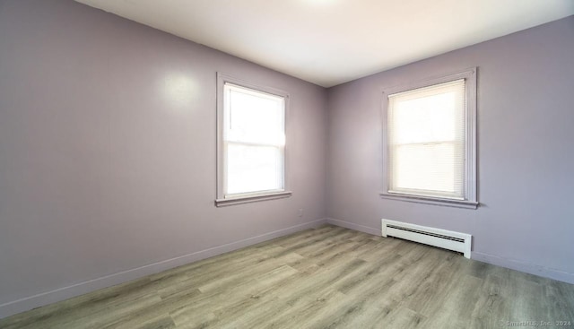 spare room featuring a healthy amount of sunlight, light hardwood / wood-style floors, and a baseboard heating unit