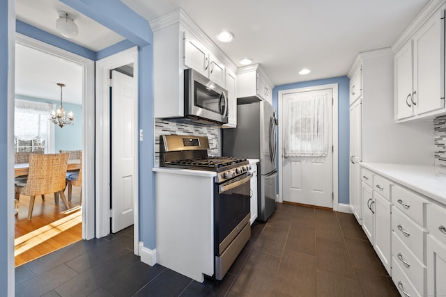 kitchen featuring appliances with stainless steel finishes, tasteful backsplash, dark wood-type flooring, a chandelier, and white cabinetry