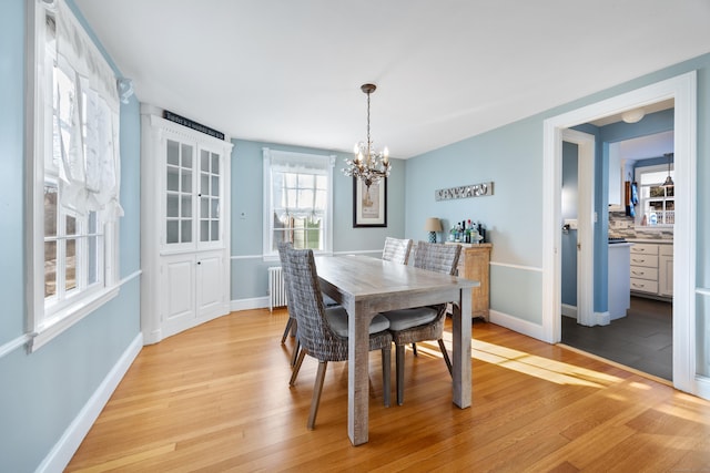 dining area with light wood-type flooring, an inviting chandelier, and radiator