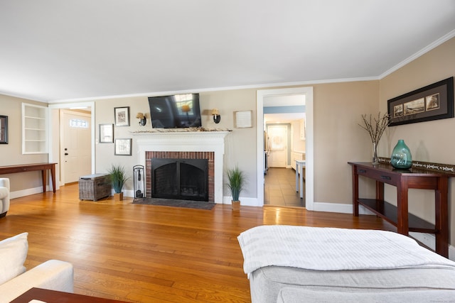 living room with built in shelves, hardwood / wood-style flooring, a brick fireplace, and crown molding