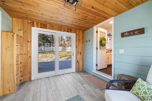 doorway to outside with wood walls, wood ceiling, and light wood-type flooring