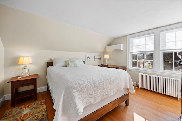 bedroom with hardwood / wood-style flooring, lofted ceiling, radiator heating unit, and a wall unit AC