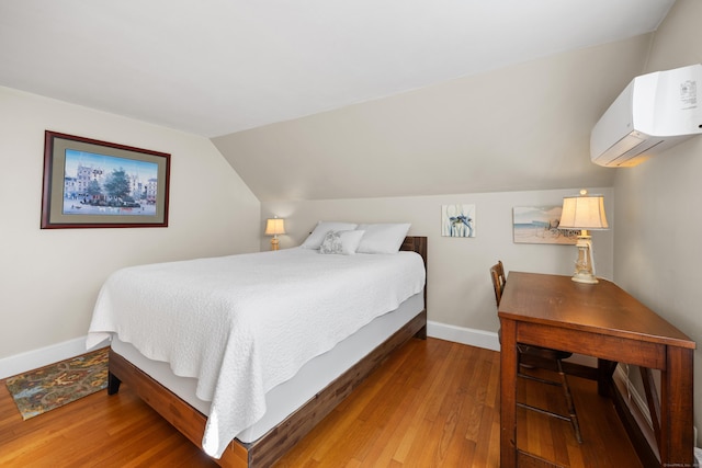 bedroom featuring wood-type flooring, vaulted ceiling, and a wall unit AC