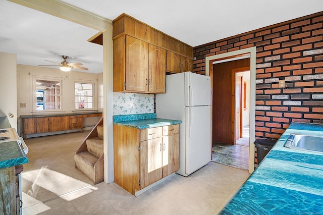 kitchen featuring ceiling fan, sink, brick wall, and white refrigerator