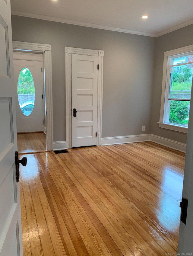 foyer entrance with light hardwood / wood-style floors, a wealth of natural light, and ornamental molding