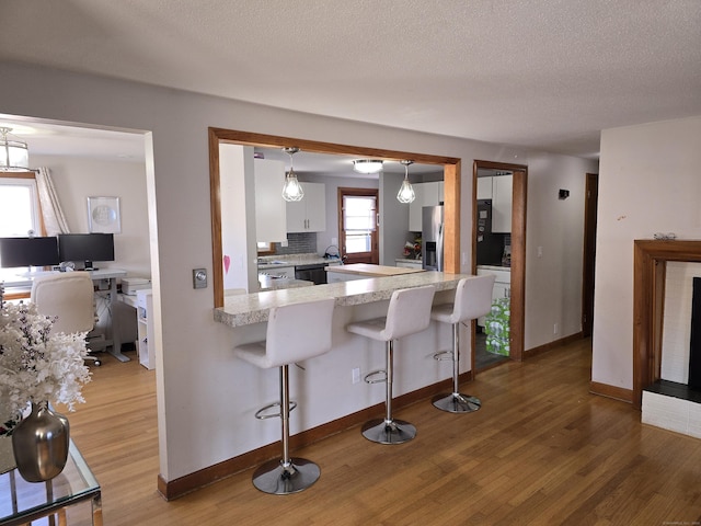 kitchen with pendant lighting, hardwood / wood-style floors, a kitchen breakfast bar, kitchen peninsula, and white cabinetry