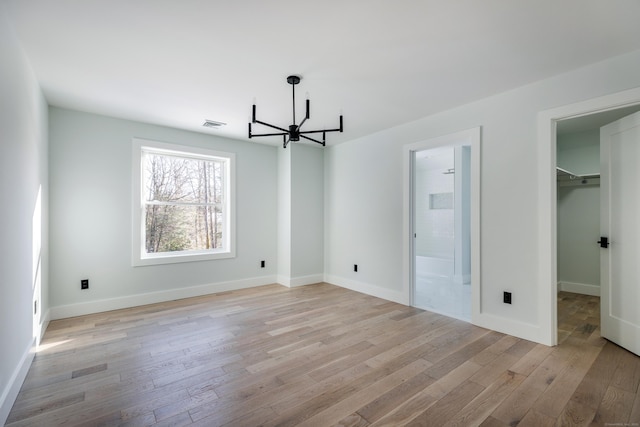 unfurnished bedroom with baseboards, a notable chandelier, a spacious closet, and light wood finished floors