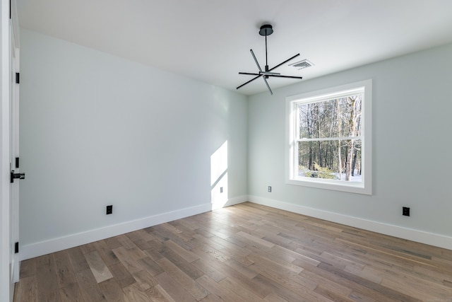 spare room featuring visible vents, a notable chandelier, baseboards, and wood finished floors