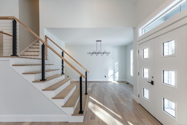 foyer entrance with a notable chandelier, a towering ceiling, wood finished floors, baseboards, and stairs