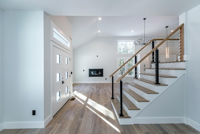 stairs with baseboards, a chandelier, wood finished floors, and a glass covered fireplace