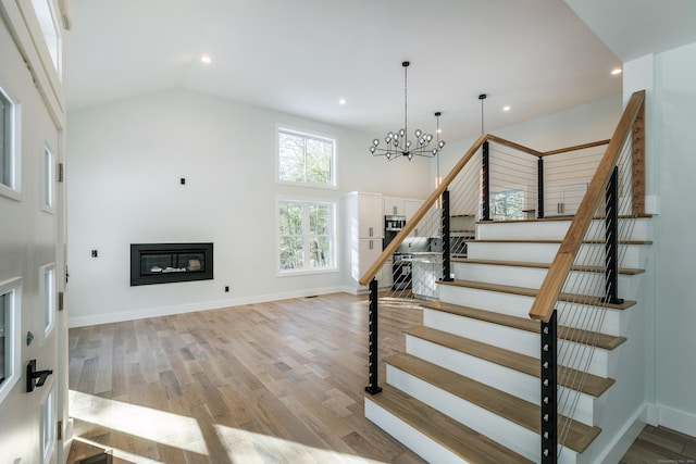 stairway featuring high vaulted ceiling, recessed lighting, wood finished floors, baseboards, and a glass covered fireplace