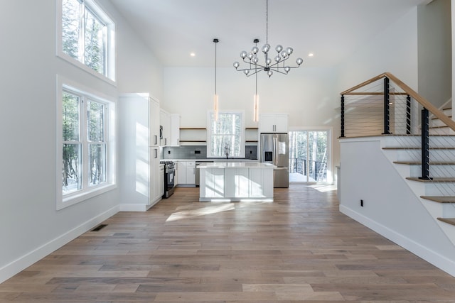 kitchen with visible vents, a kitchen island, appliances with stainless steel finishes, a high ceiling, and light wood-type flooring