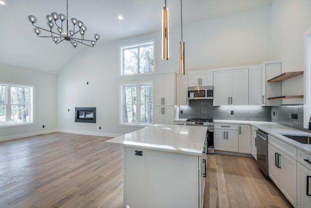 kitchen with high vaulted ceiling, appliances with stainless steel finishes, open shelves, and a glass covered fireplace