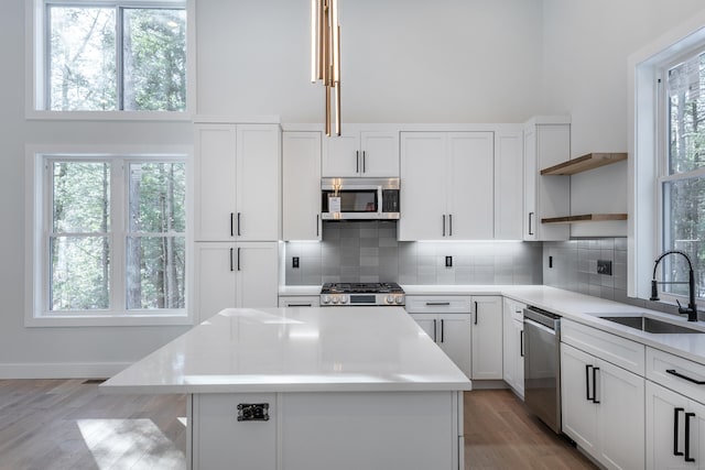 kitchen with stainless steel appliances, a sink, a towering ceiling, backsplash, and open shelves