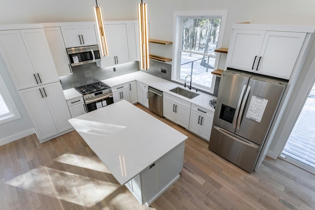 kitchen featuring a sink, light wood-style floors, appliances with stainless steel finishes, decorative backsplash, and open shelves