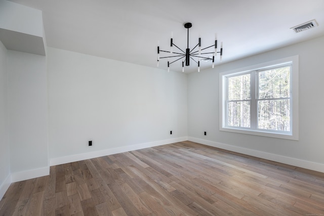 unfurnished room featuring an inviting chandelier, visible vents, baseboards, and wood finished floors