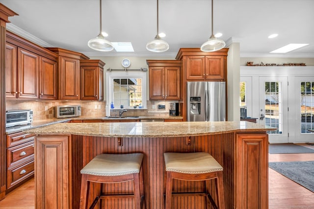 kitchen with stainless steel fridge with ice dispenser, a skylight, light hardwood / wood-style flooring, and sink