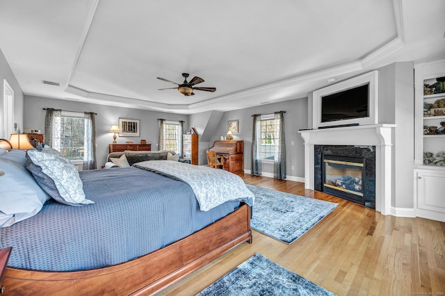 bedroom with multiple windows, light hardwood / wood-style floors, ceiling fan, and a premium fireplace