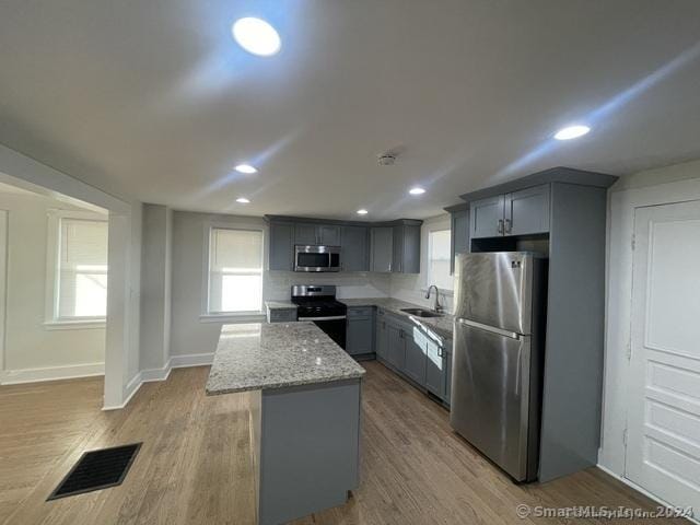 kitchen with light stone countertops, appliances with stainless steel finishes, a center island, and light hardwood / wood-style floors