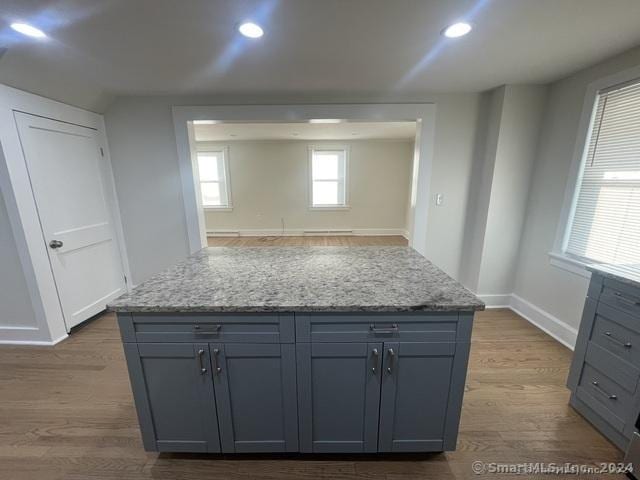 kitchen with hardwood / wood-style floors, gray cabinets, light stone counters, and a kitchen island