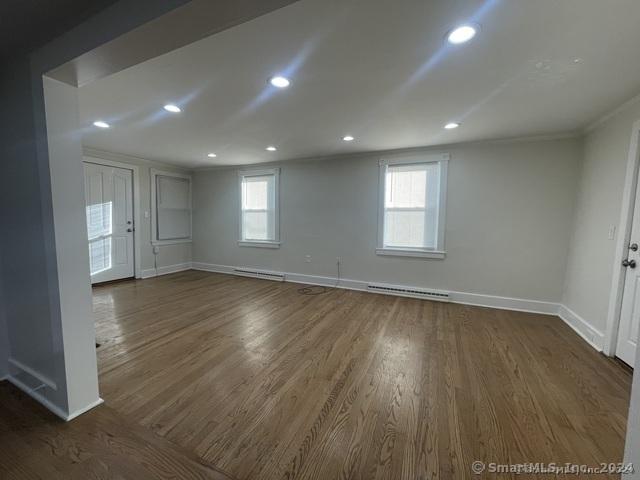 unfurnished room with plenty of natural light, dark wood-type flooring, and a baseboard heating unit