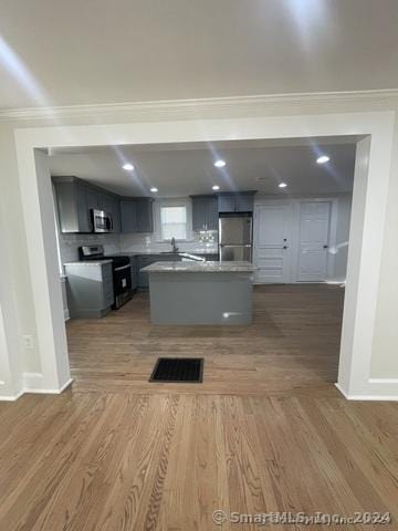 kitchen featuring a center island, crown molding, decorative backsplash, appliances with stainless steel finishes, and dark hardwood / wood-style flooring