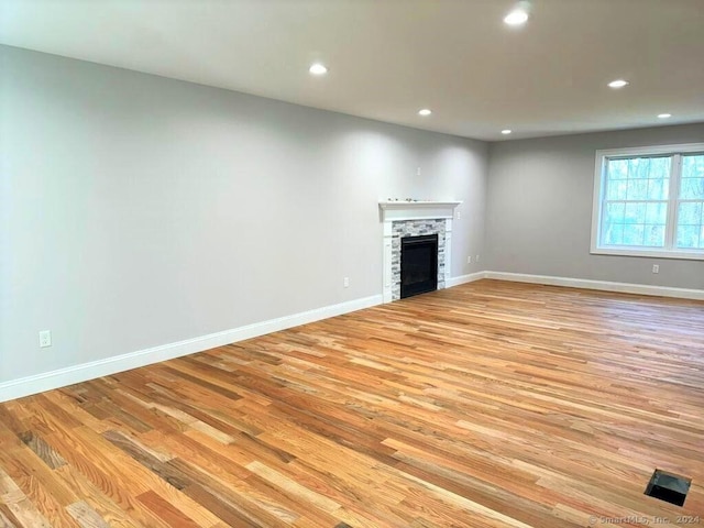 unfurnished living room featuring a stone fireplace and light hardwood / wood-style flooring