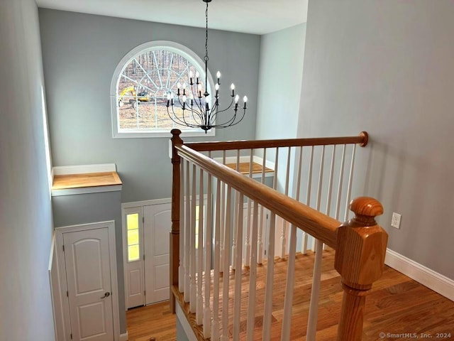 stairway with hardwood / wood-style floors and an inviting chandelier