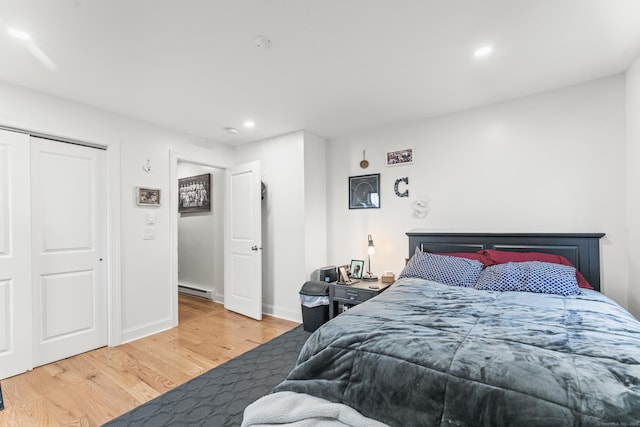 bedroom with hardwood / wood-style floors, a baseboard heating unit, and a closet