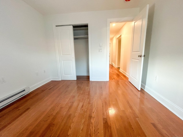 unfurnished bedroom with a closet, baseboard heating, and light hardwood / wood-style floors