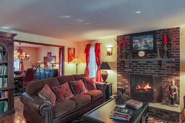 living room featuring a brick fireplace, an inviting chandelier, a textured ceiling, and hardwood / wood-style flooring