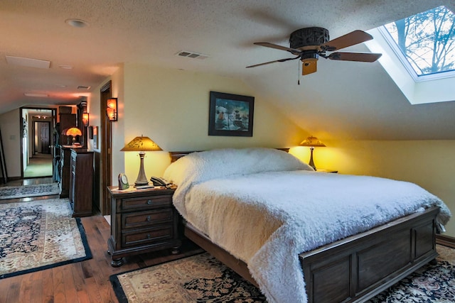 bedroom featuring a textured ceiling, ceiling fan, lofted ceiling with skylight, and dark hardwood / wood-style floors