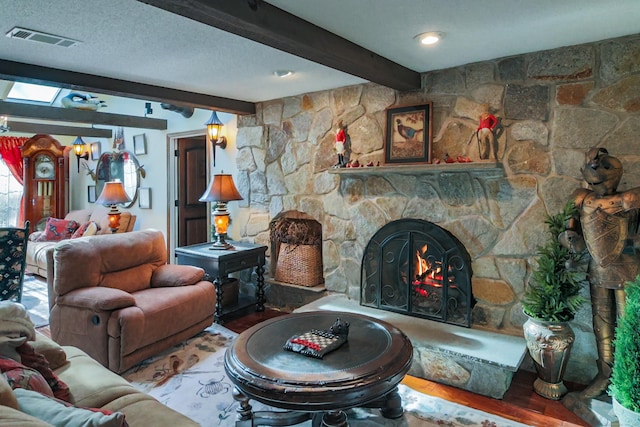 living room featuring beamed ceiling, a stone fireplace, wood-type flooring, and a textured ceiling