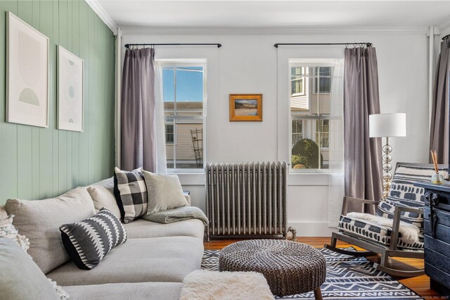 living room with radiator heating unit, hardwood / wood-style floors, crown molding, and wood walls