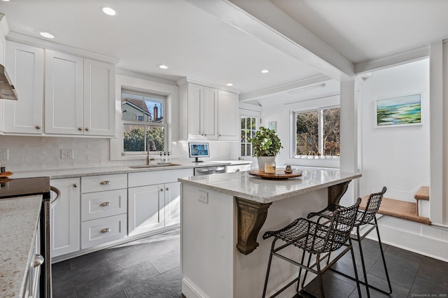kitchen featuring appliances with stainless steel finishes, white cabinetry, a sink, a breakfast bar area, and backsplash